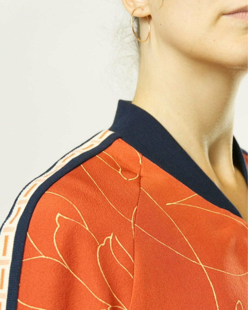 Nahansicht von Frau mit ziegelroter Bomberjacke aus Kimono mit gelben Chrysanthemen in Linienform. Fokus auf dunkelblauen Kragen und auf Zierband auf den Ärmeln