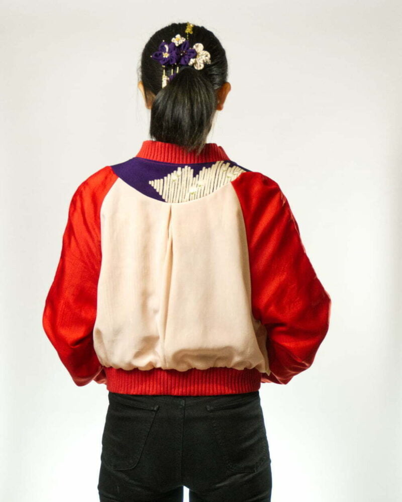 Hinteransicht von Frau mit links herum getragener Bomberjacke aus Kimono, bestehend aus rot-weissem Seidenfutter und lila Beleg mit weissen Streifenmustern, weissen und rosa Kirschblüten mit goldenen Akzenten und Bündchen aus rotem, grobgeripptem Baumwollrundstrick
