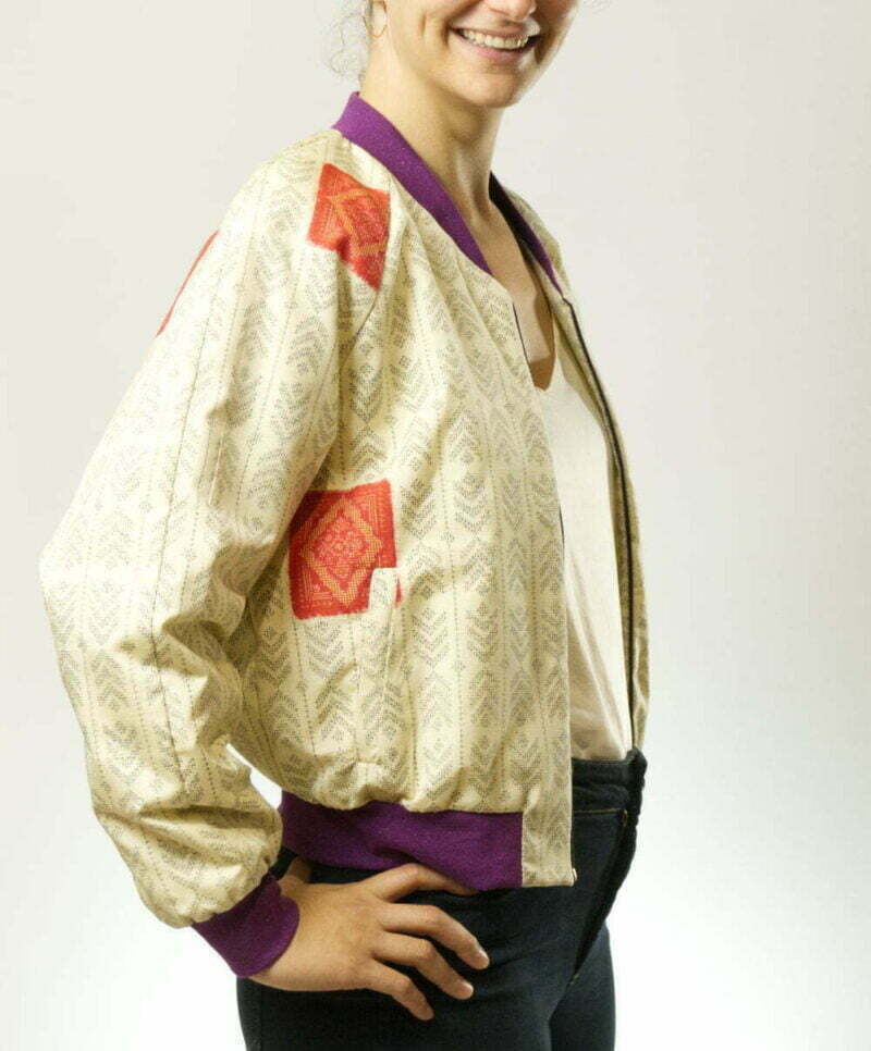 Seitenansicht von Frau mit ecrufarbener Bomberjacke aus Kimono mit Pfeilfedern als Muster, lila Glitzerbündchen und seitlichen Eingrifftaschen