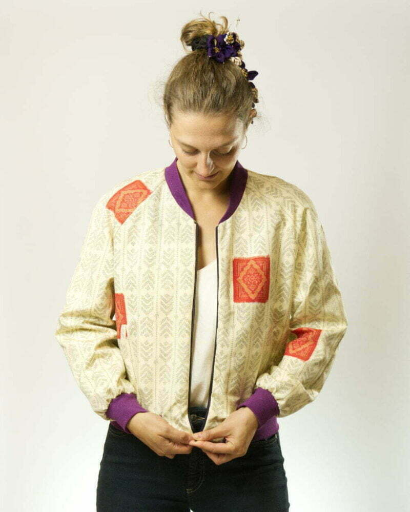 Vorderansicht von Frau mit offener, ecrufarbener Bomberjacke aus Kimono mit Pfeilfedern als Muster und lila Glitzerbündchen