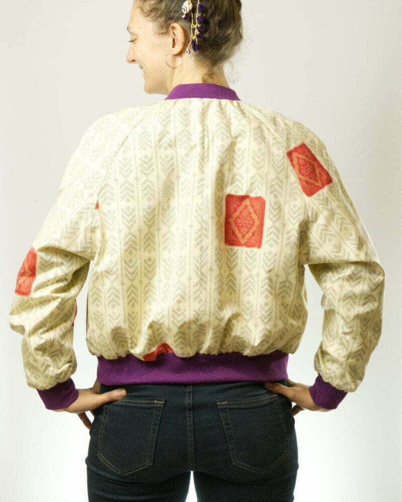 Hinteransicht von Frau mit ecrufarbener Bomberjacke aus Kimono mit Pfeilfedern als Muster und lila Glitzerbündchen