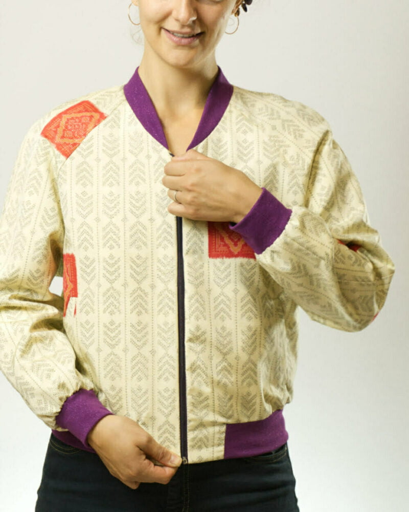 Vorderansicht von Frau mit geschlossener, ecrufarbener Bomberjacke aus Kimono mit Pfeilfedern als Muster und lila Glitzerbündchen